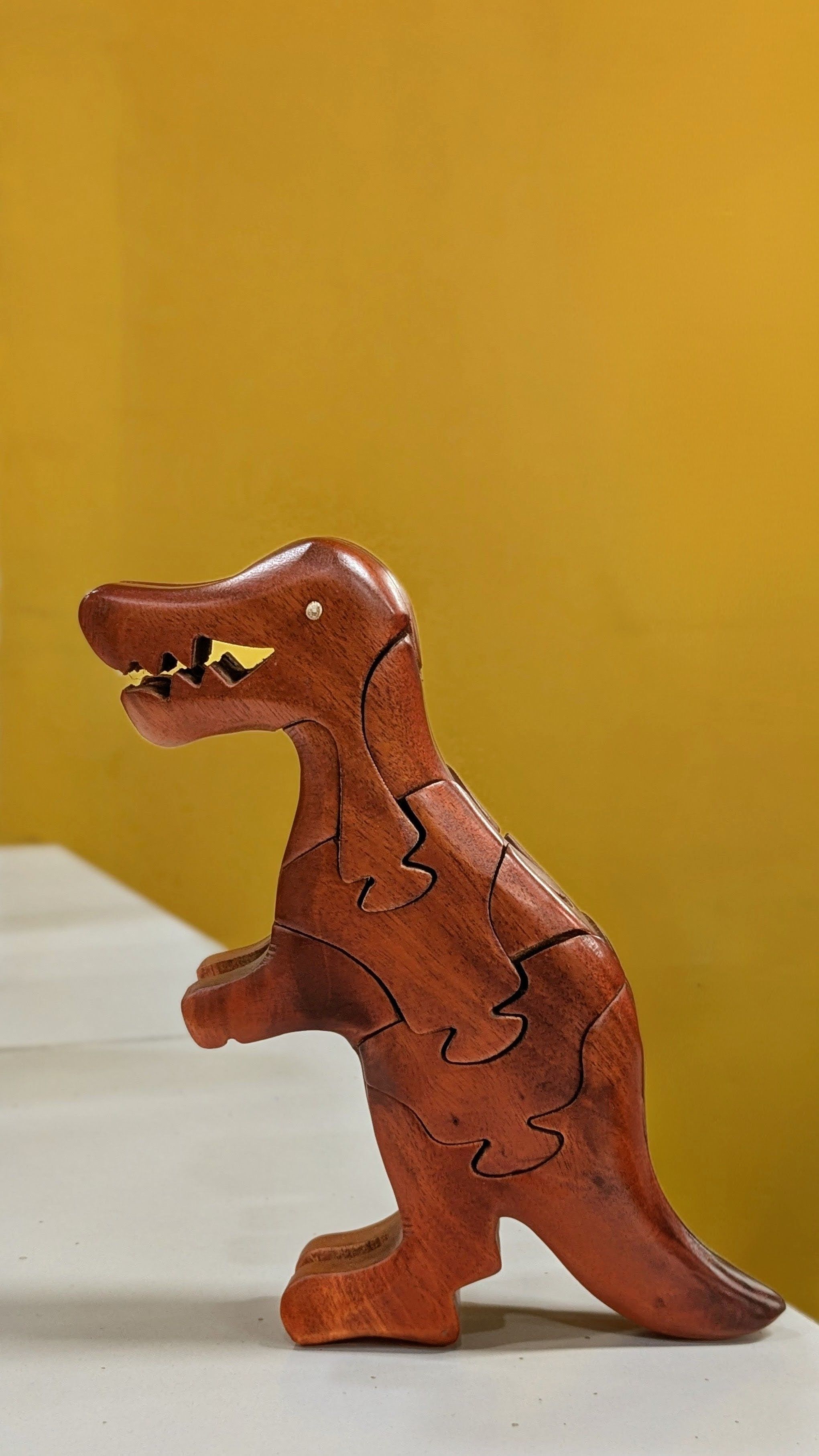 A handcrafted wooden dinosaur puzzle stands against a vibrant yellow backdrop.