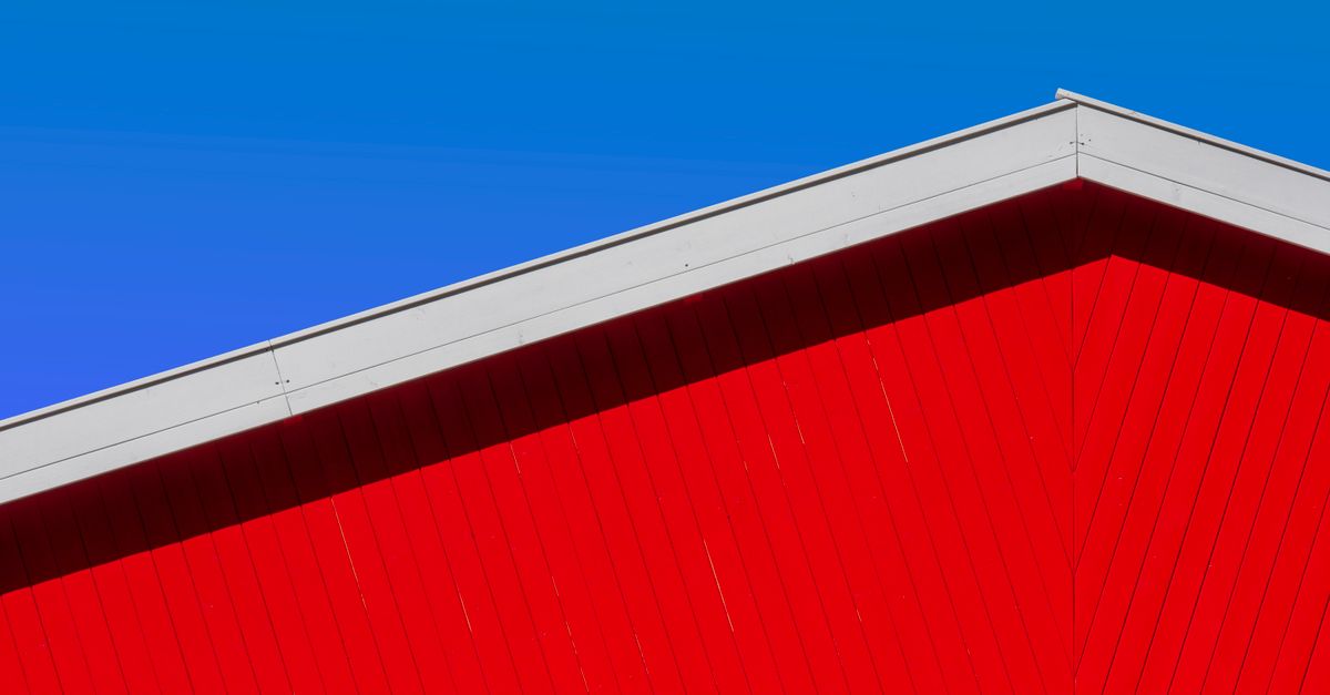 Striking red barn roof set against a vibrant blue sky, showcasing minimalist architectural design.