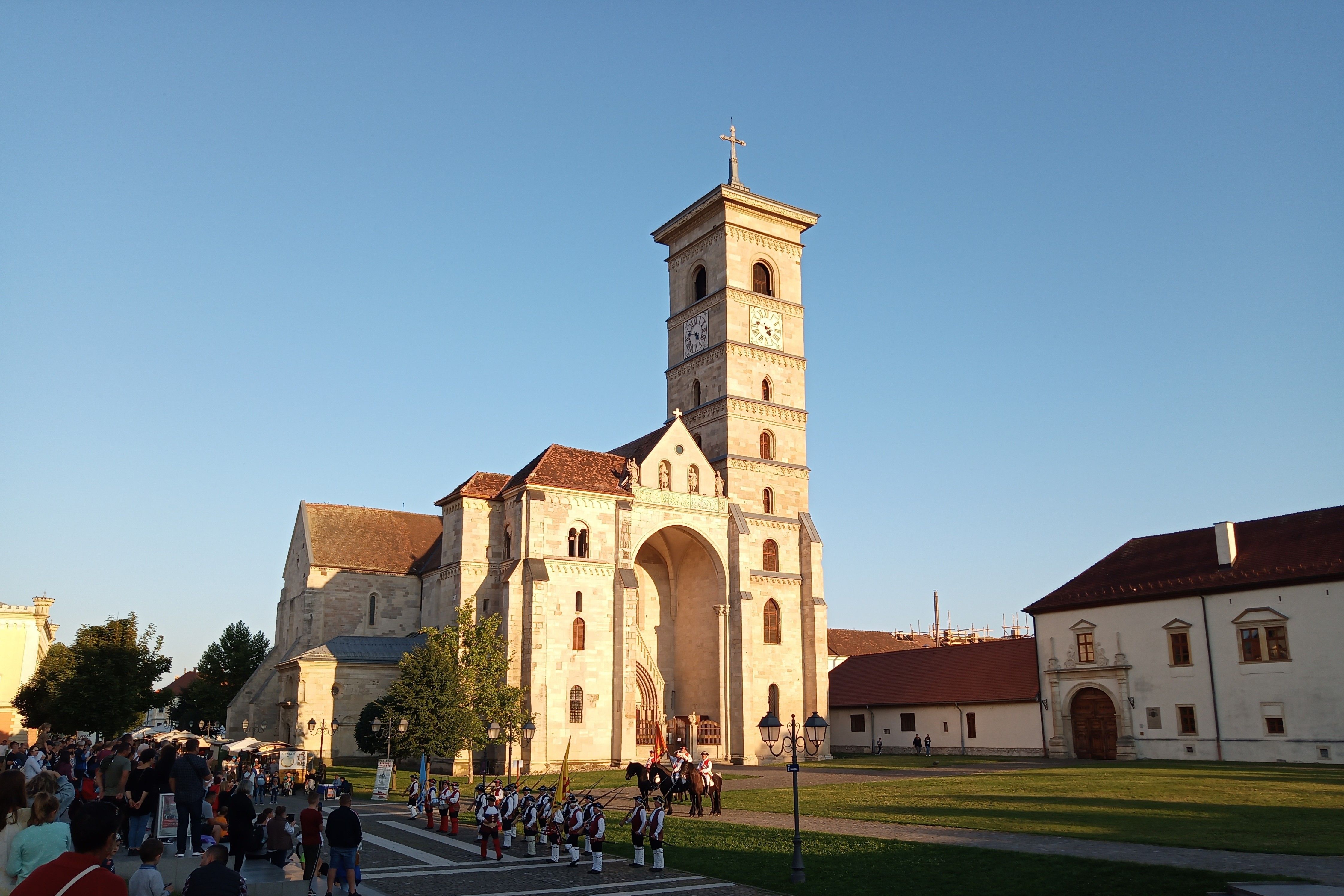 A statue of a saint with a gathering crowd at sunset in a European town square.