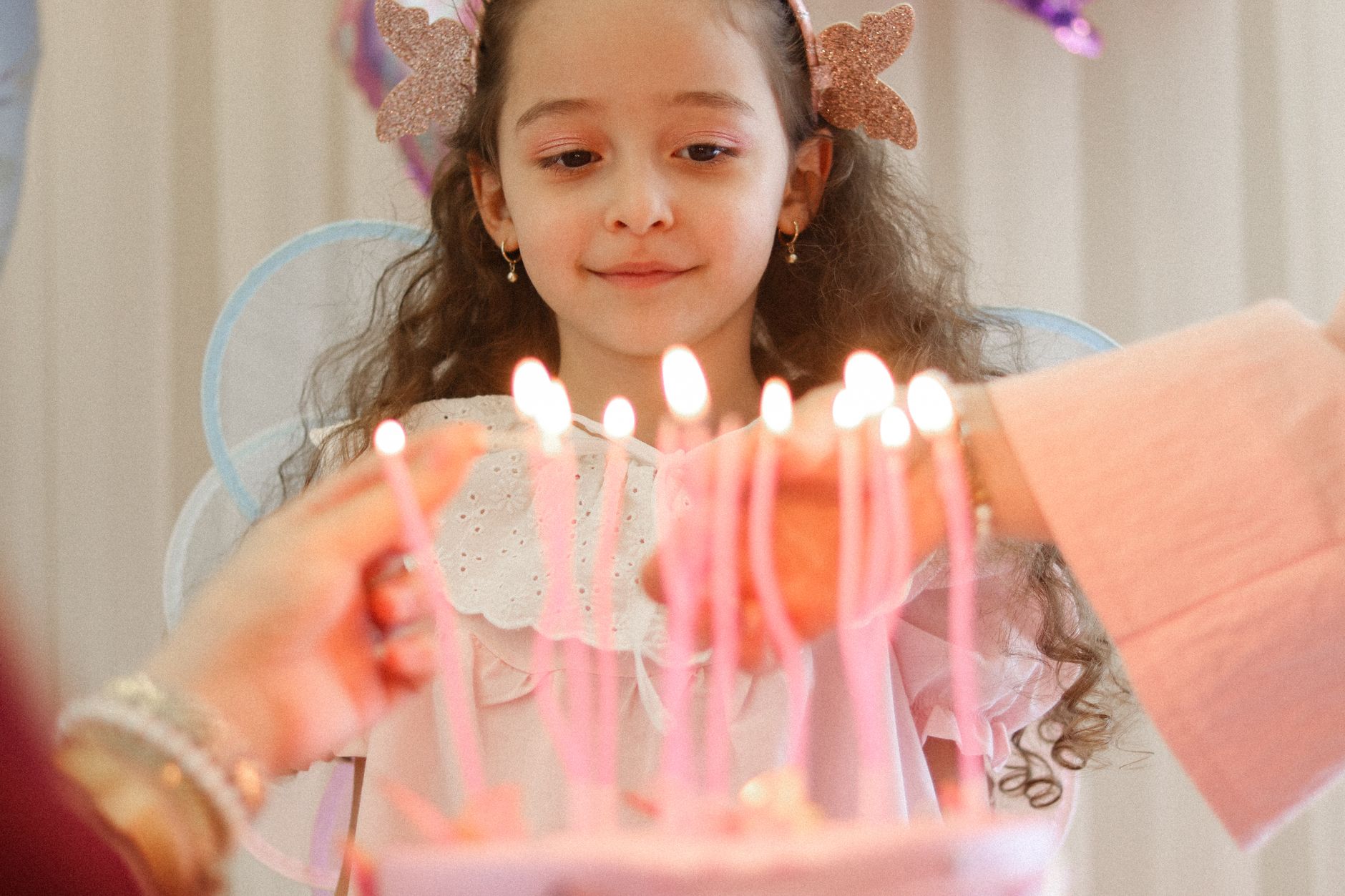 Charming young girl in a fairy costume delighting in her birthday cake with lit candles indoors.
