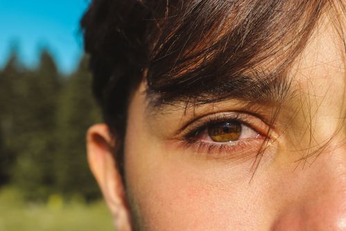 Free A detailed close-up photo of a young man's eye with a natural outdoor background. Stock Photo