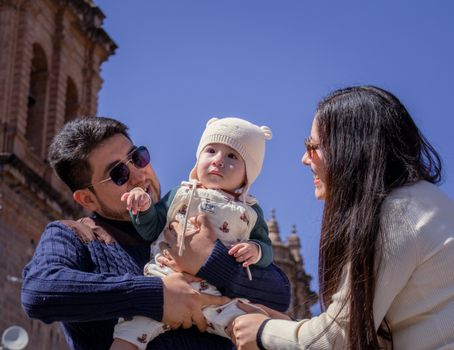 Happy family with a baby enjoying a sunny day in front of a historic building, capturing joyful moments.