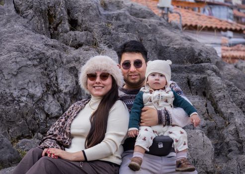 Family seated on rocks wearing warm clothing, capturing a cozy autumn moment outdoors.