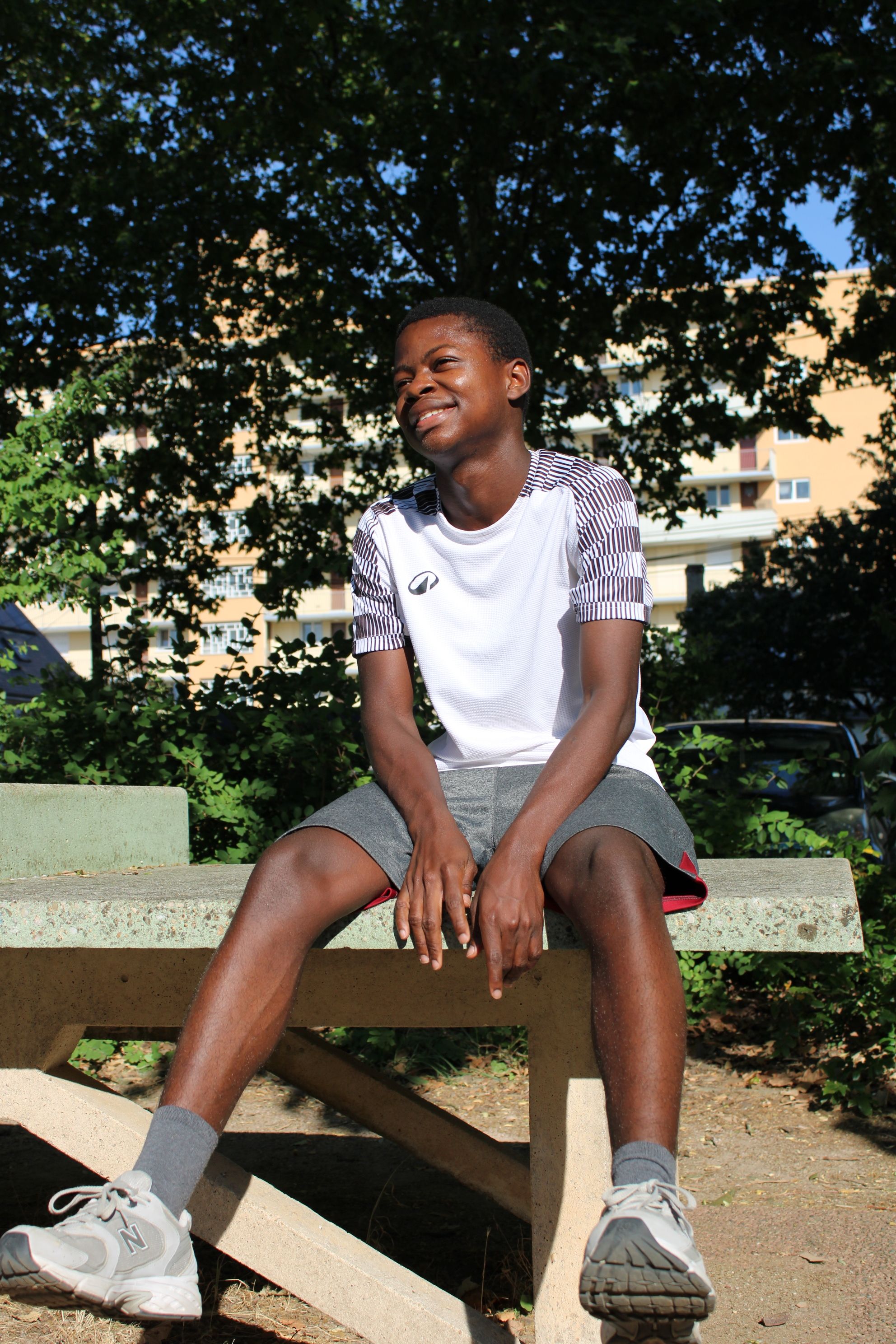 Smiling teen sitting on a concrete bench outdoors on a sunny day.