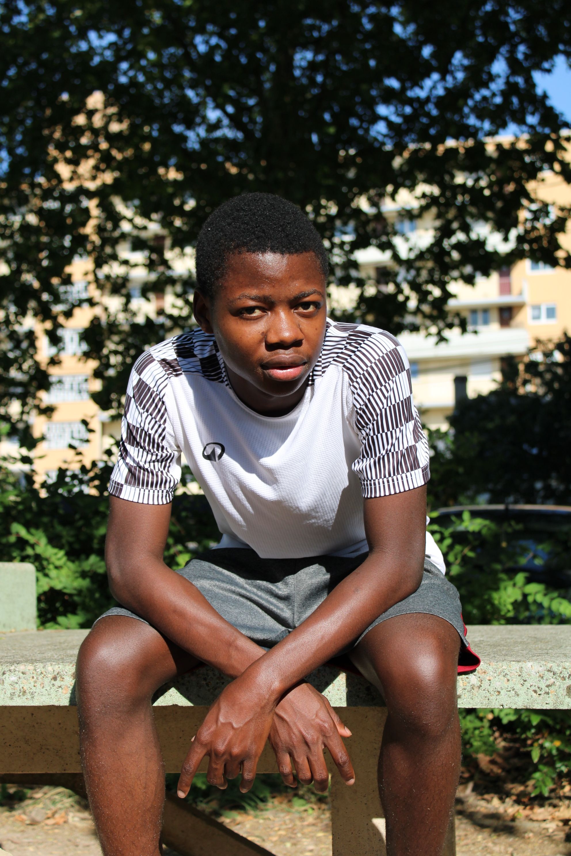 A young man sitting on a bench outdoors during a sunny day.