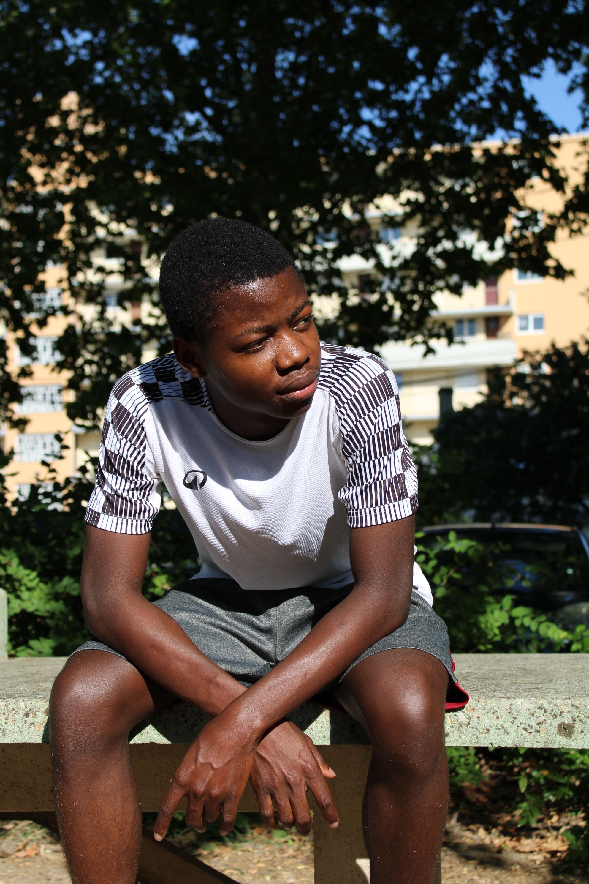 Teenage boy sitting on a park bench enjoying a sunny day outdoors in an urban area.