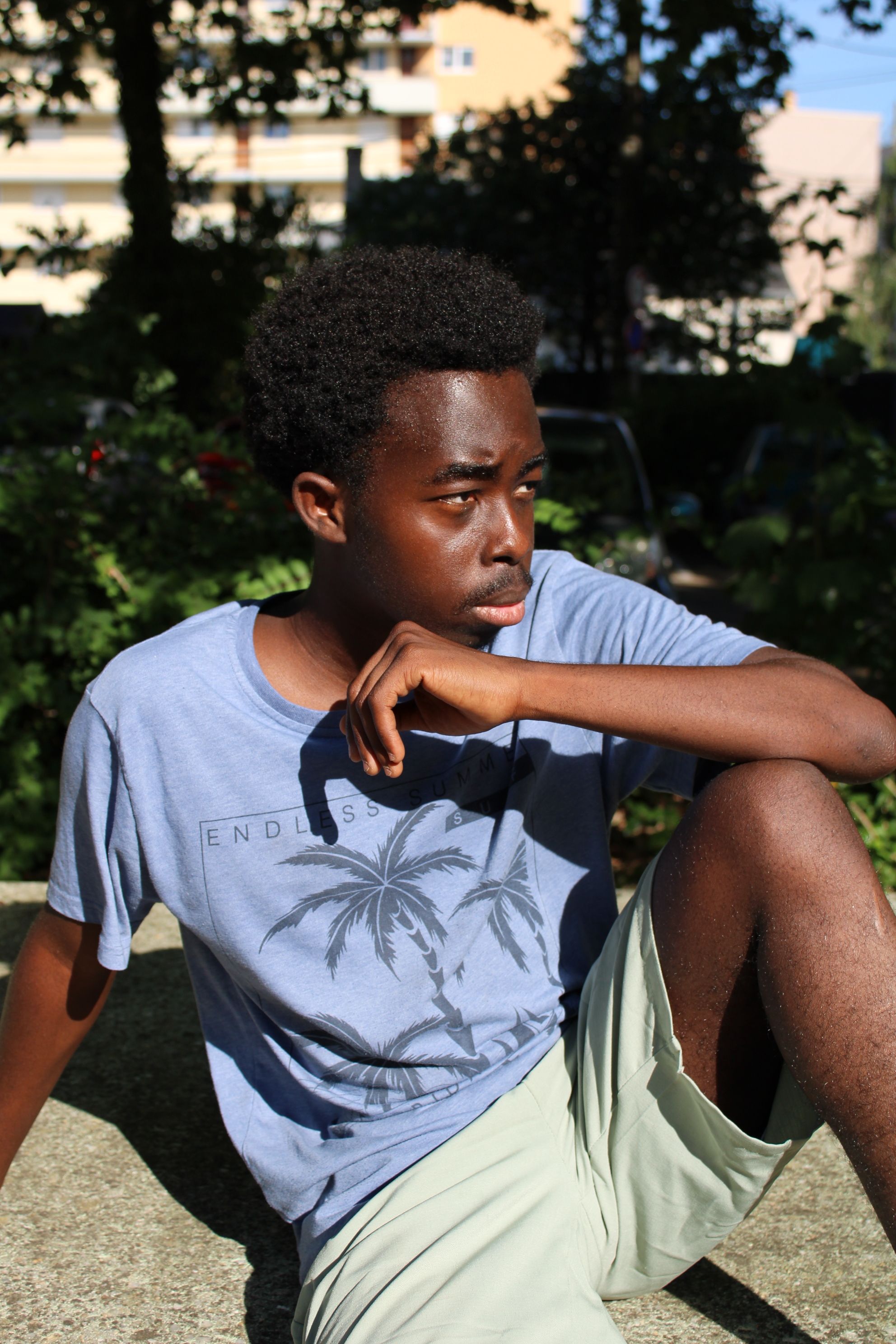 Casual portrait of a young man sitting in a sunny park, reflecting thoughtfully.