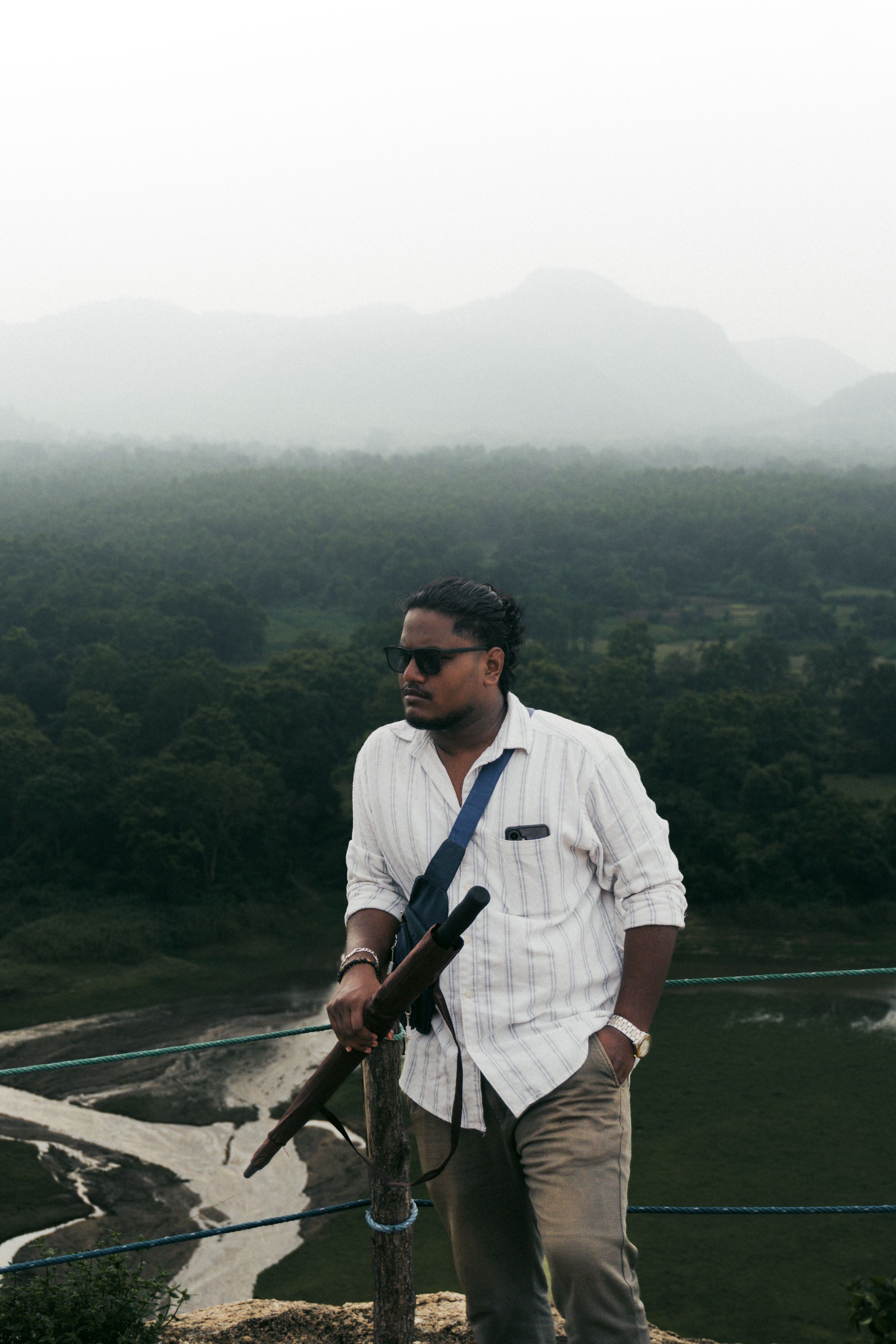 Man standing on a hilltop, admiring a lush green valley with distant mountains.