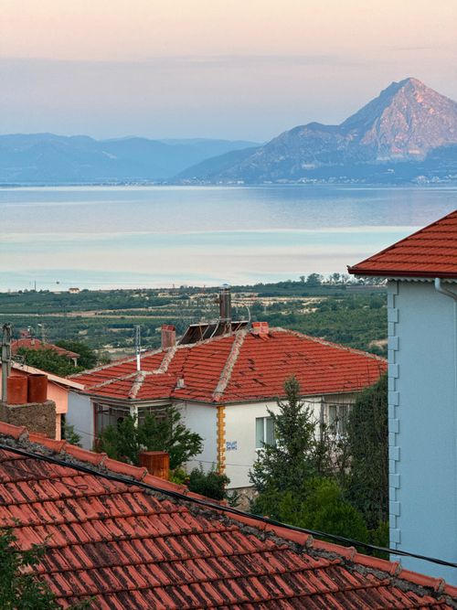 Free Charming Turkish village with red roofs and mountain backdrop at sunset, featuring lakeside tranquility. Stock Photo
