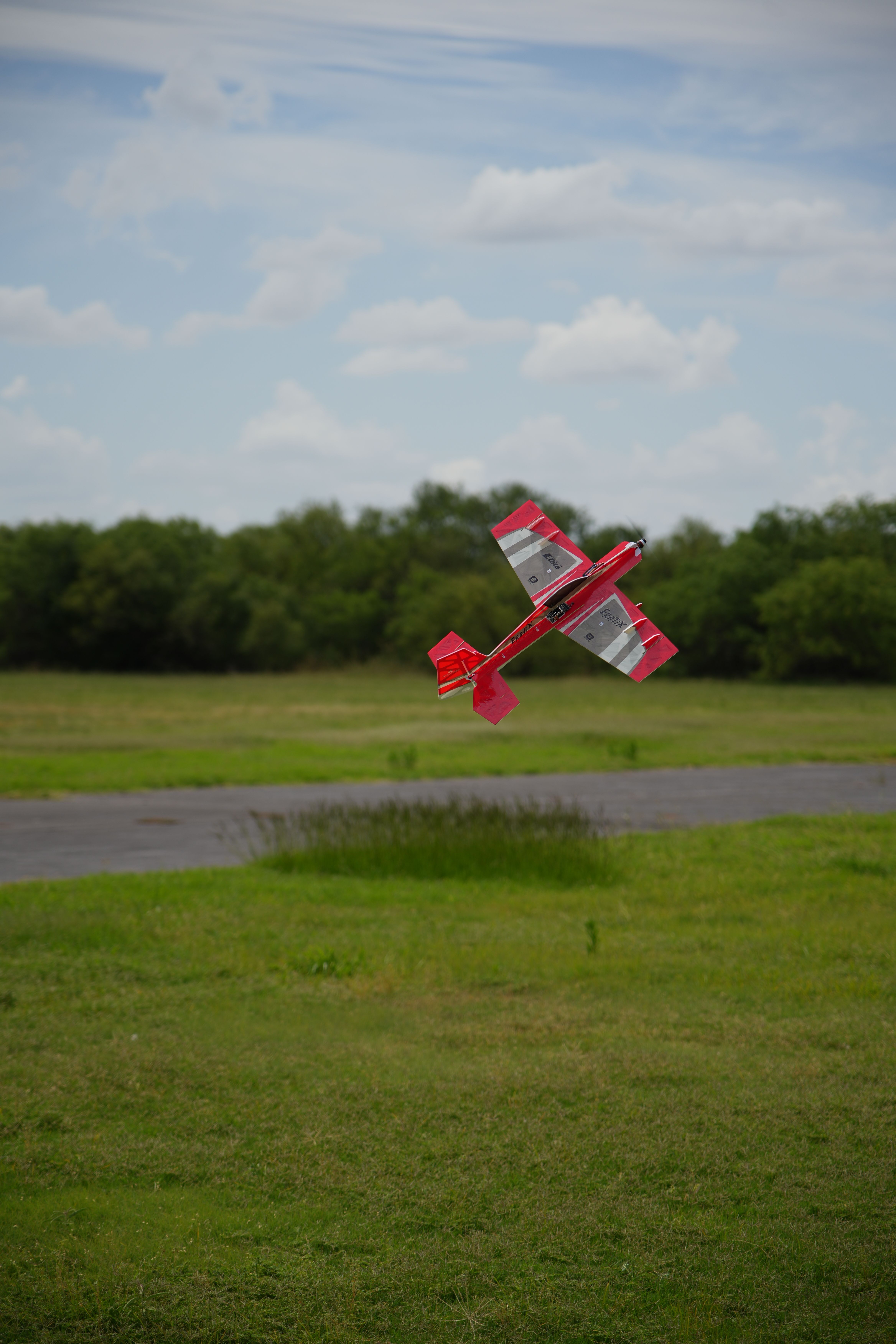 A red RC plane glides over a green field in Wichita Falls, Texas.