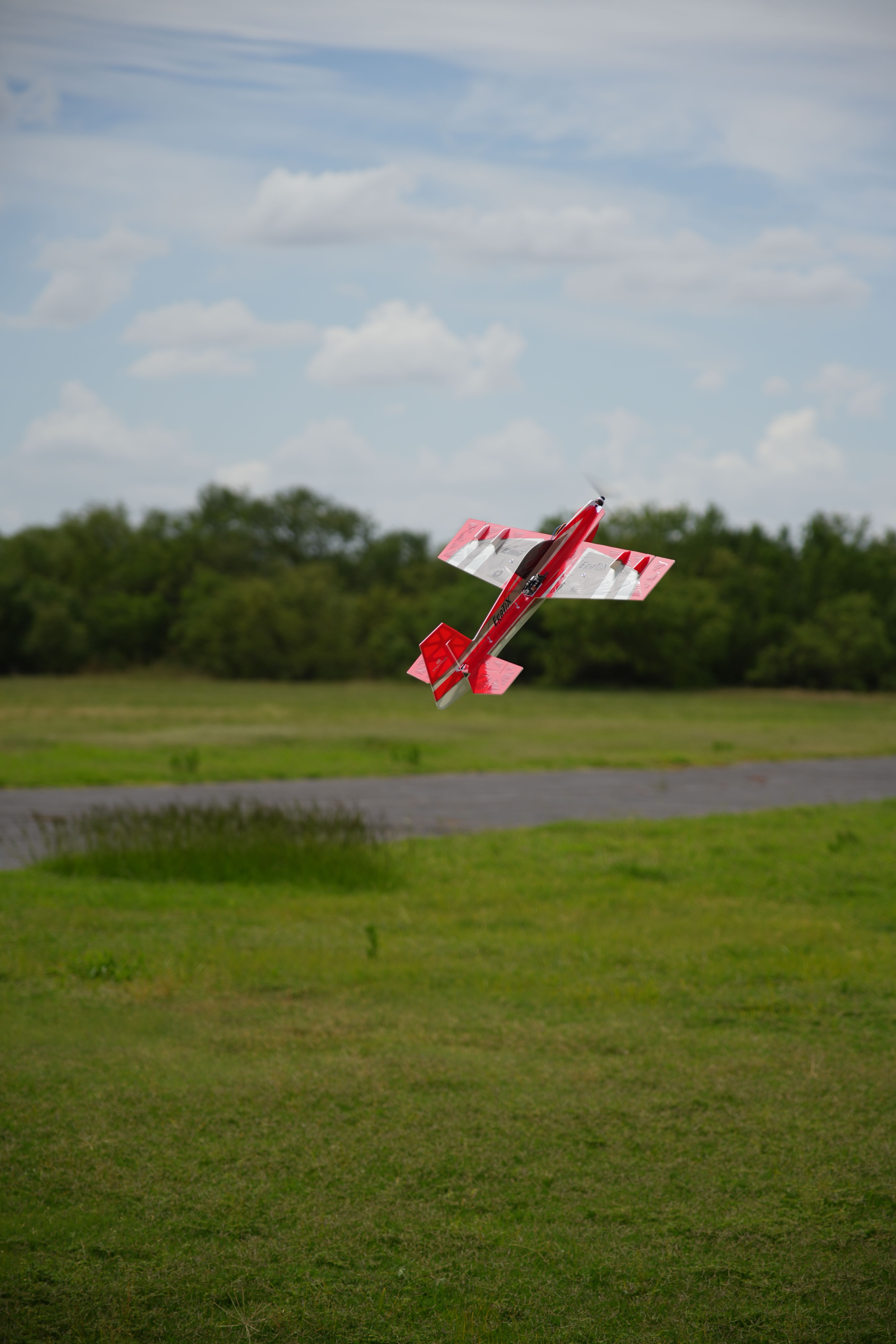 Red remote control plane soars over a green field in Wichita Falls, Texas, under a cloudy sky.