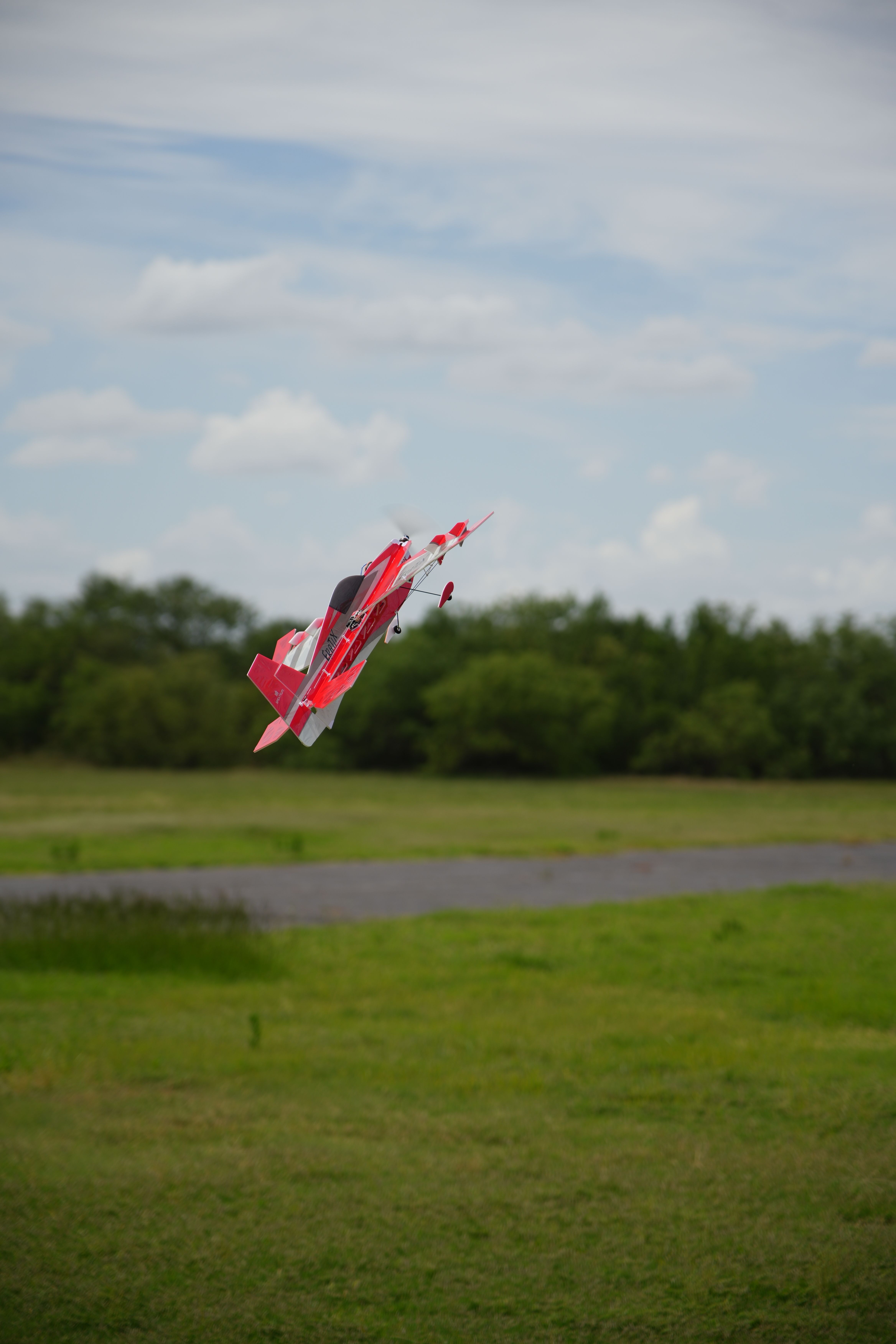 Red and white RC plane flying over a grassy field in Wichita Falls, Texas, under a clear sky.