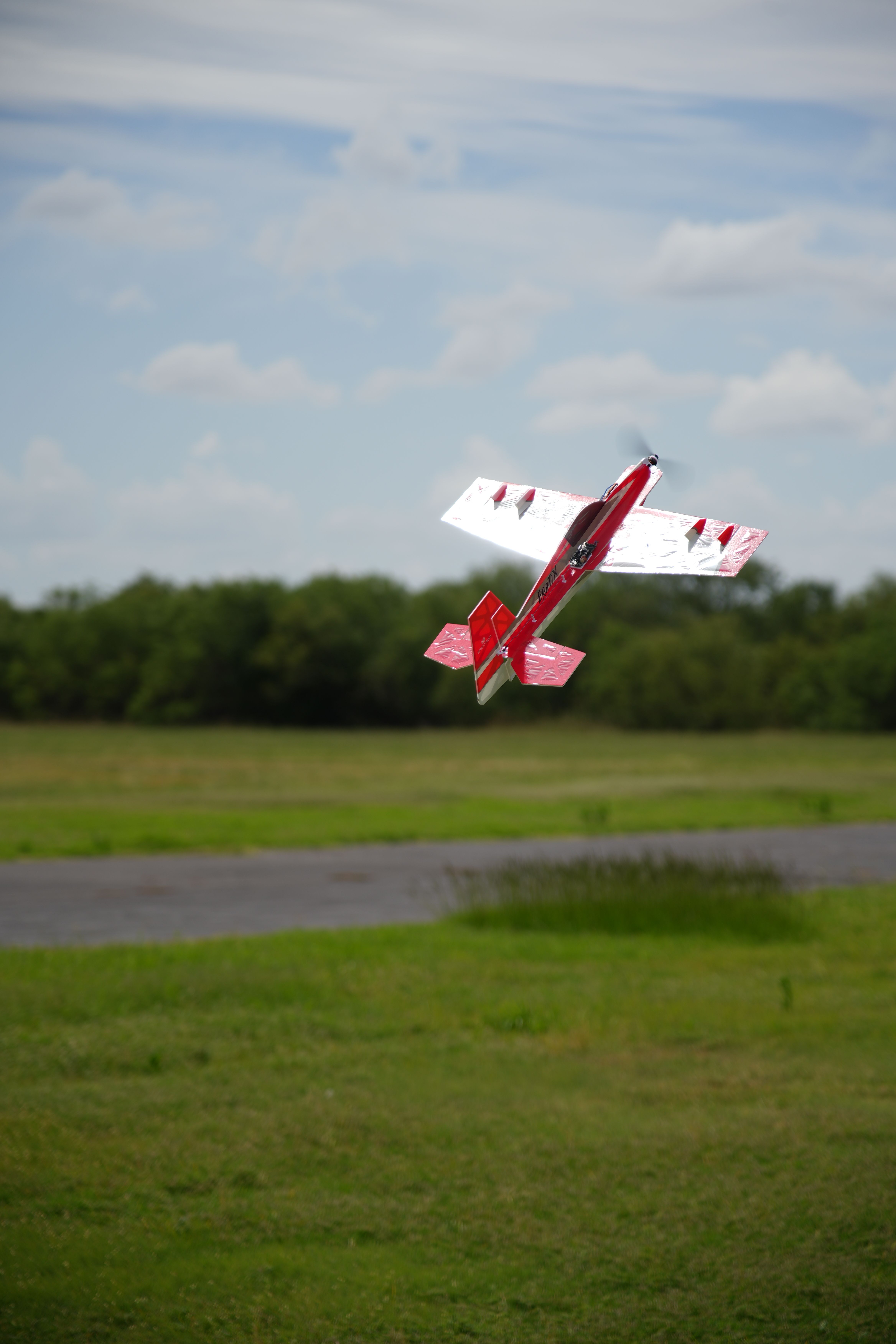 A dynamic aerial shot of a red model plane soaring above greenery in Wichita Falls, Texas.