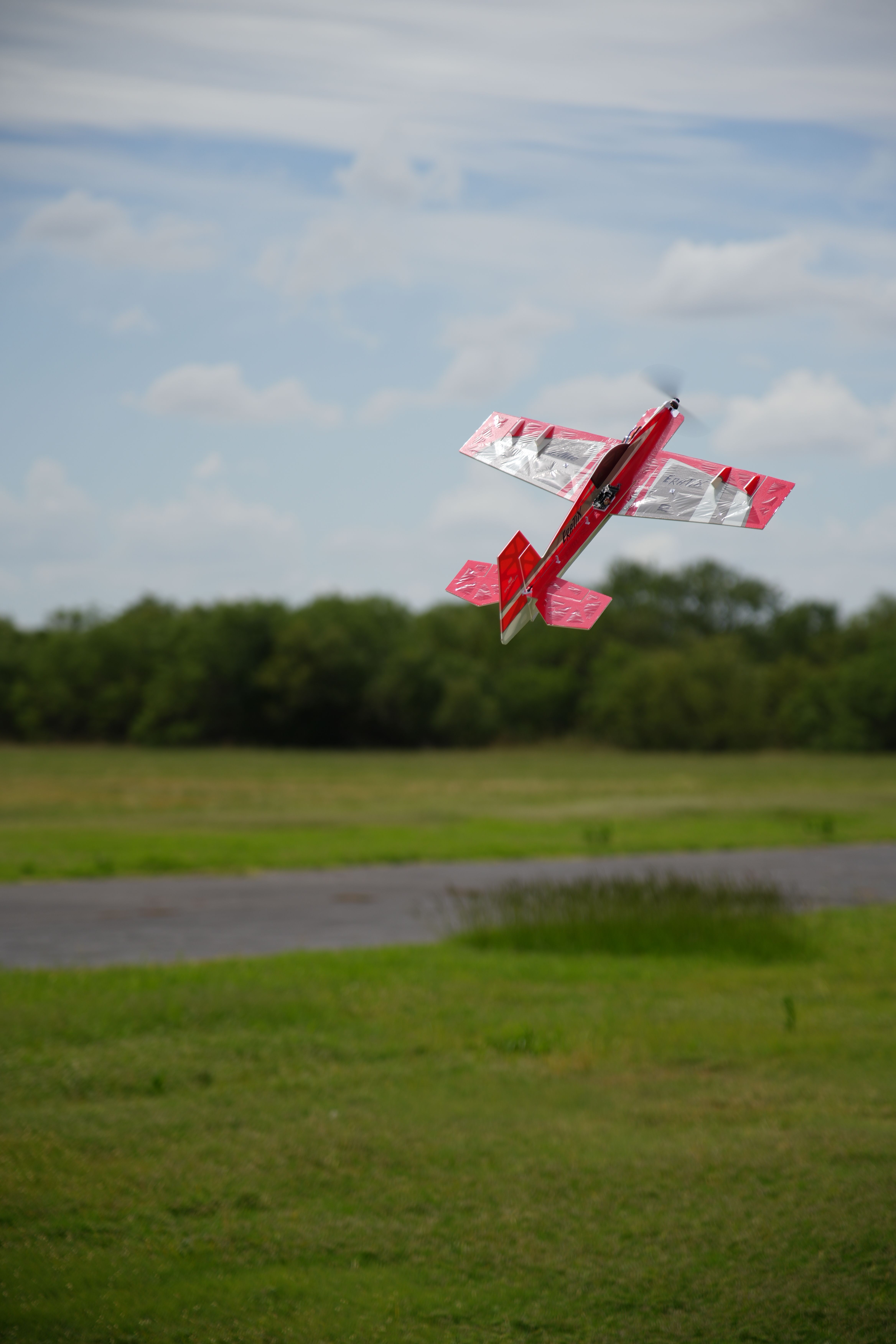 A red RC plane acrobatically soars over a grassy field in Wichita Falls.