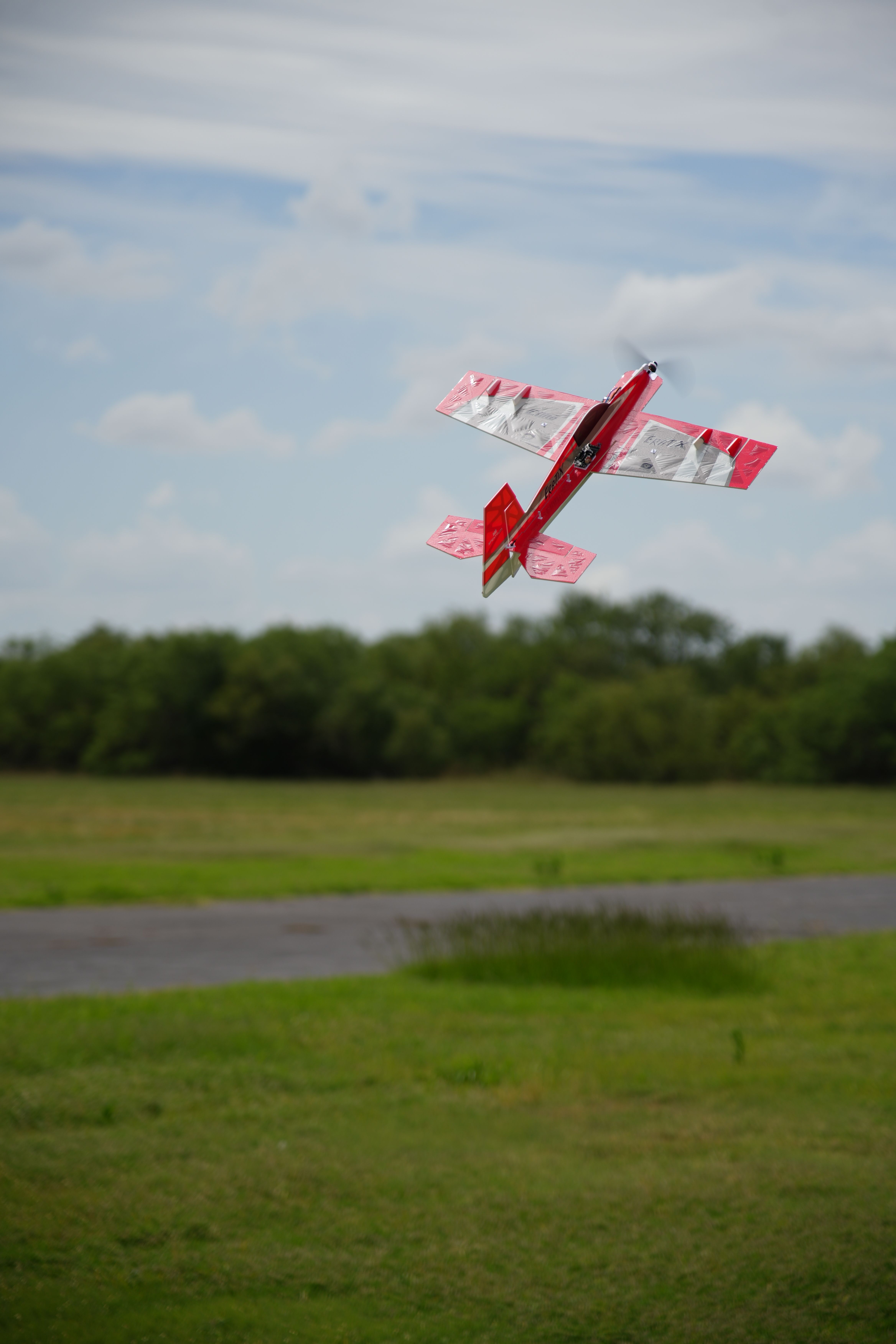 A vibrant red radio-controlled plane performs maneuvers against a blue sky in Wichita Falls, Texas.