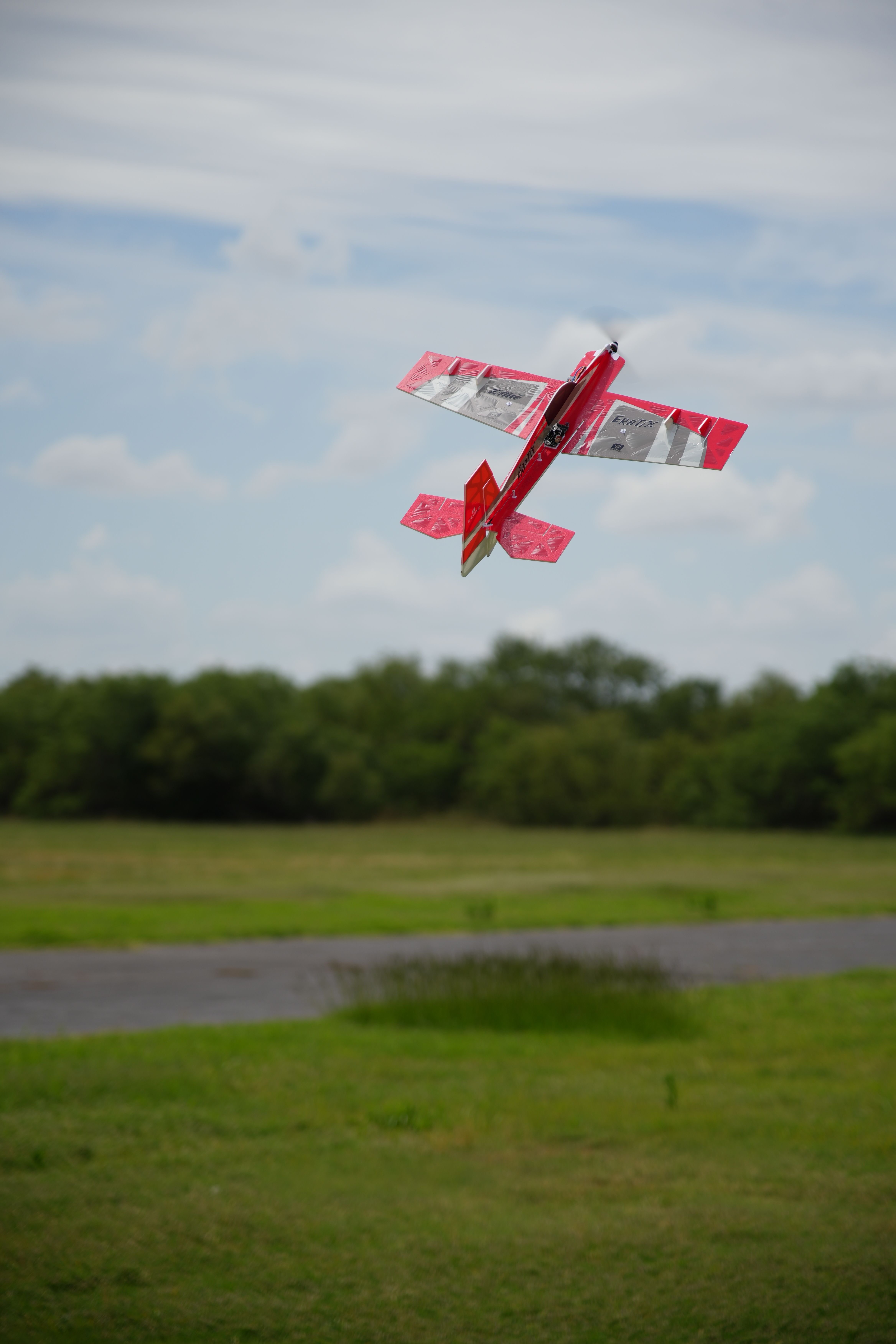 A vibrant red RC plane flying over a green field in Wichita Falls, Texas.