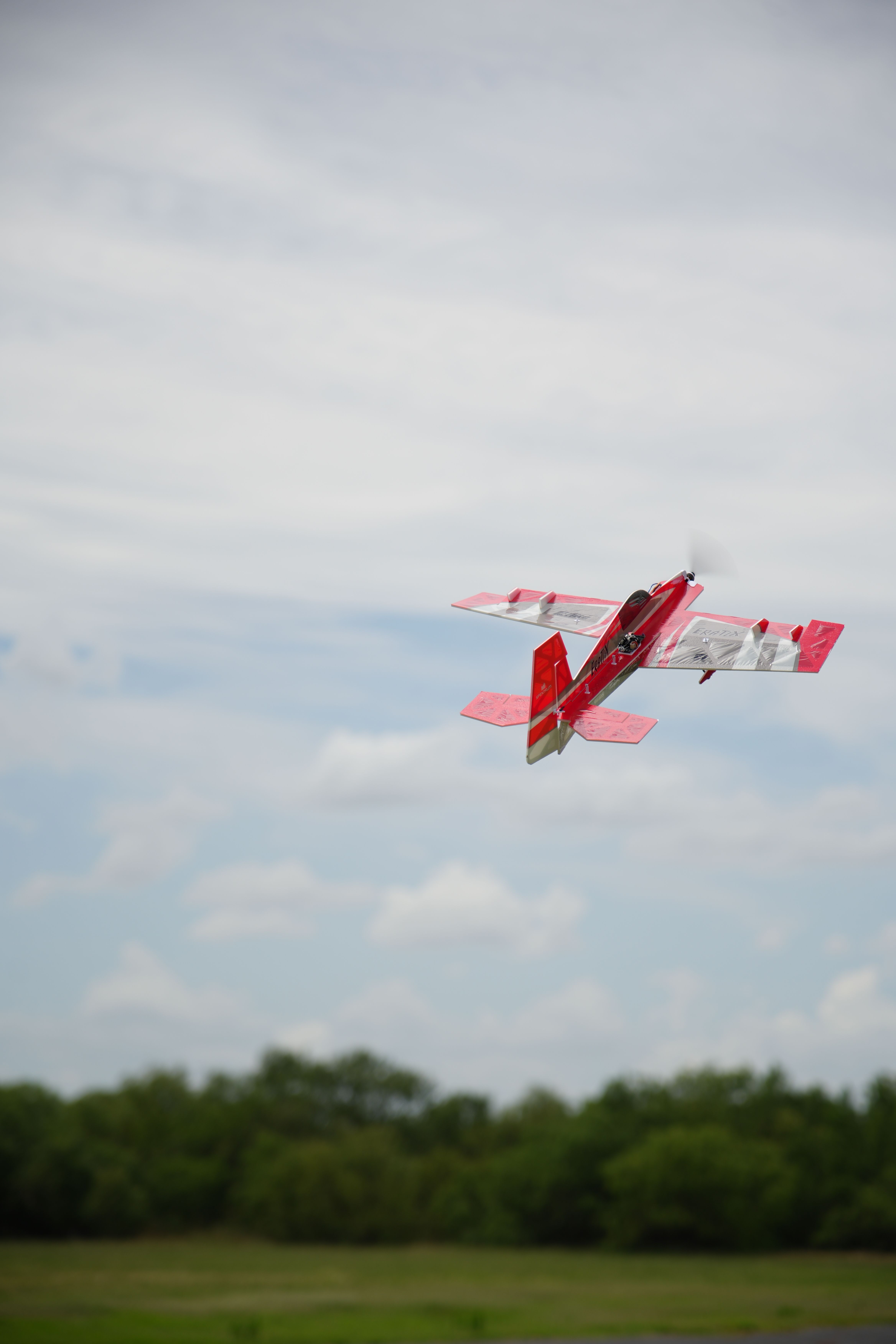 Vibrant red RC plane flying against a cloudy blue sky in Wichita Falls, Texas.