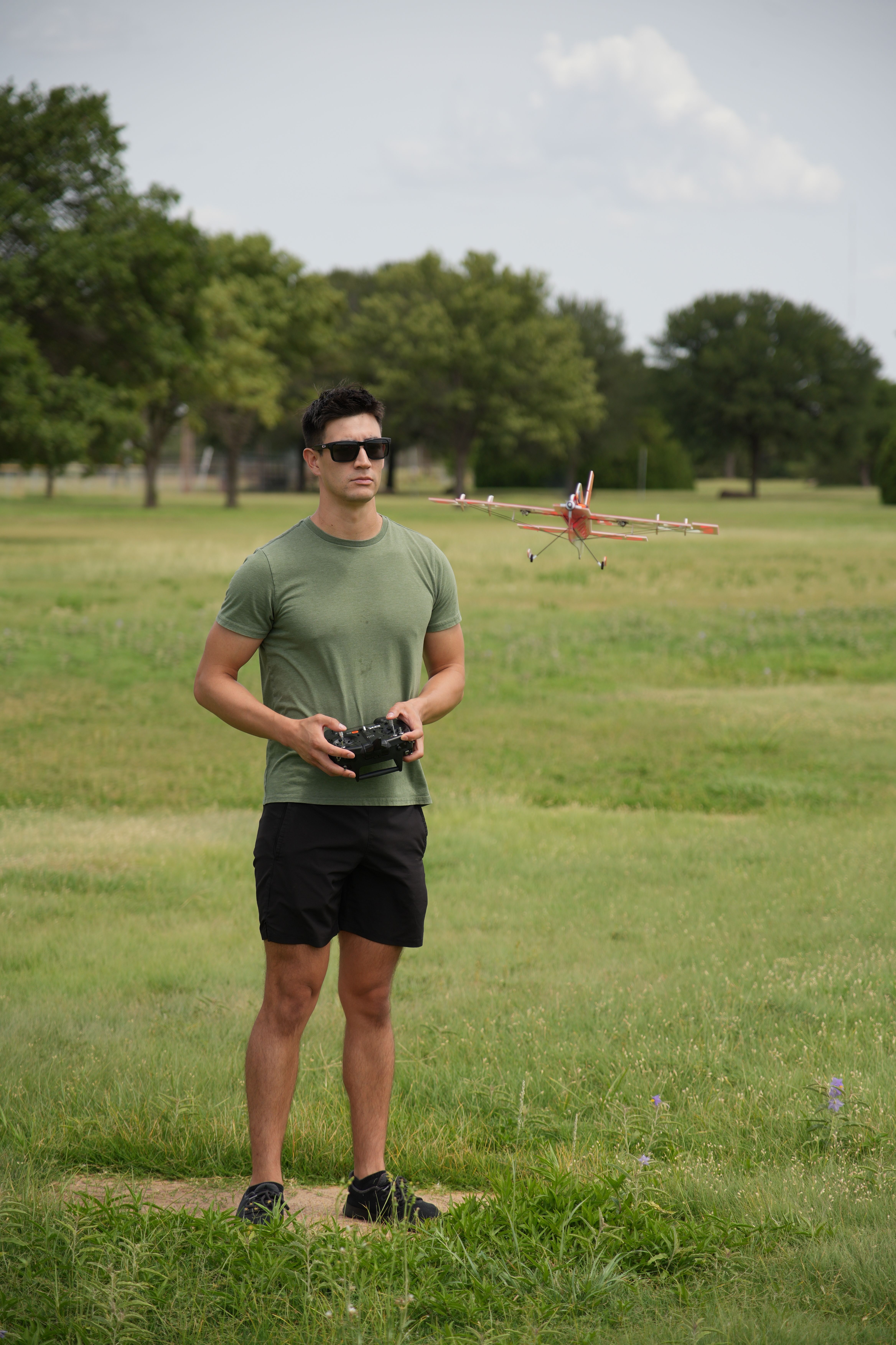 Adult male enjoying RC plane flying in Wichita Falls park with clear sky and greenery.