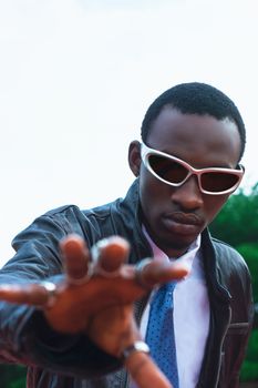 Confident man in sunglasses reaching towards the camera, exuding style and attitude.