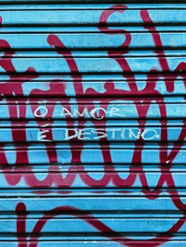 Vibrant street graffiti on a blue metal shutter with Portuguese text adding urban flair.