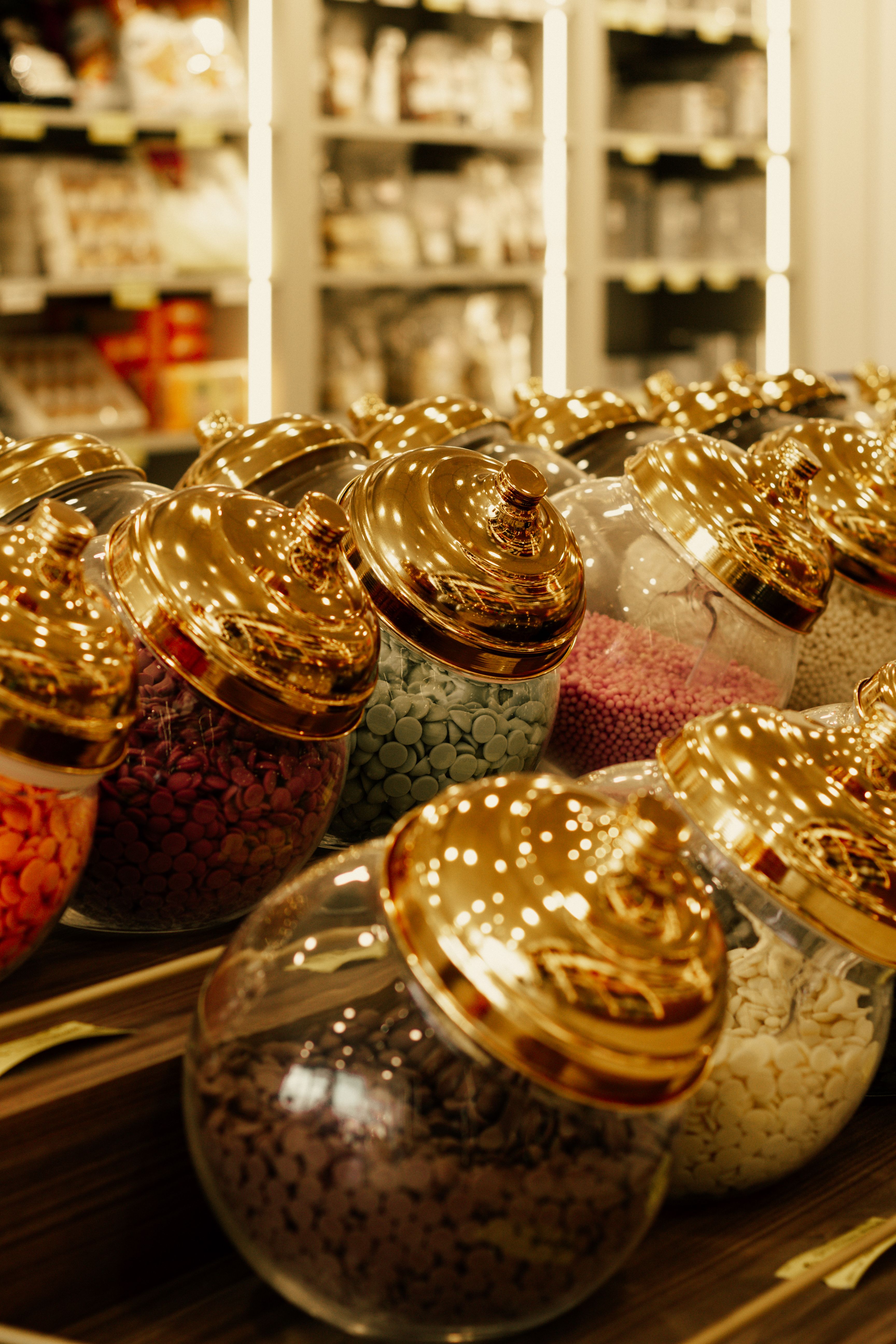 A row of candy jars with luxurious gold lids in a stylish gourmet shop setting.