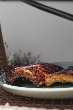 Juicy grilled barbecue ribs placed on a green plate outdoors in the sunlight.