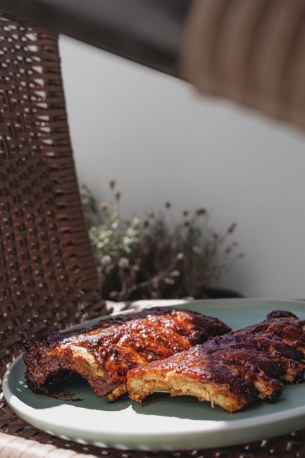A pile of glazed pork riblets on a wire rack, each piece showing a cross-section of rib bone with a thin layer of meat and dark sticky sauce coating the surface.