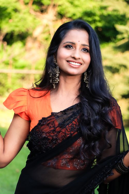 Free Smiling woman in black sari with orange blouse, enjoying sunny day outdoors. Stock Photo