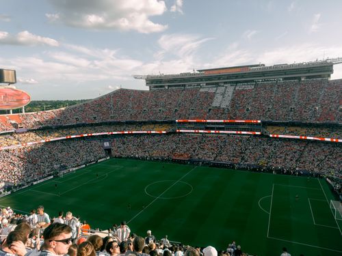 Free Aerial view of a lively soccer match in a bustling outdoor stadium filled with enthusiastic fans. Stock Photo