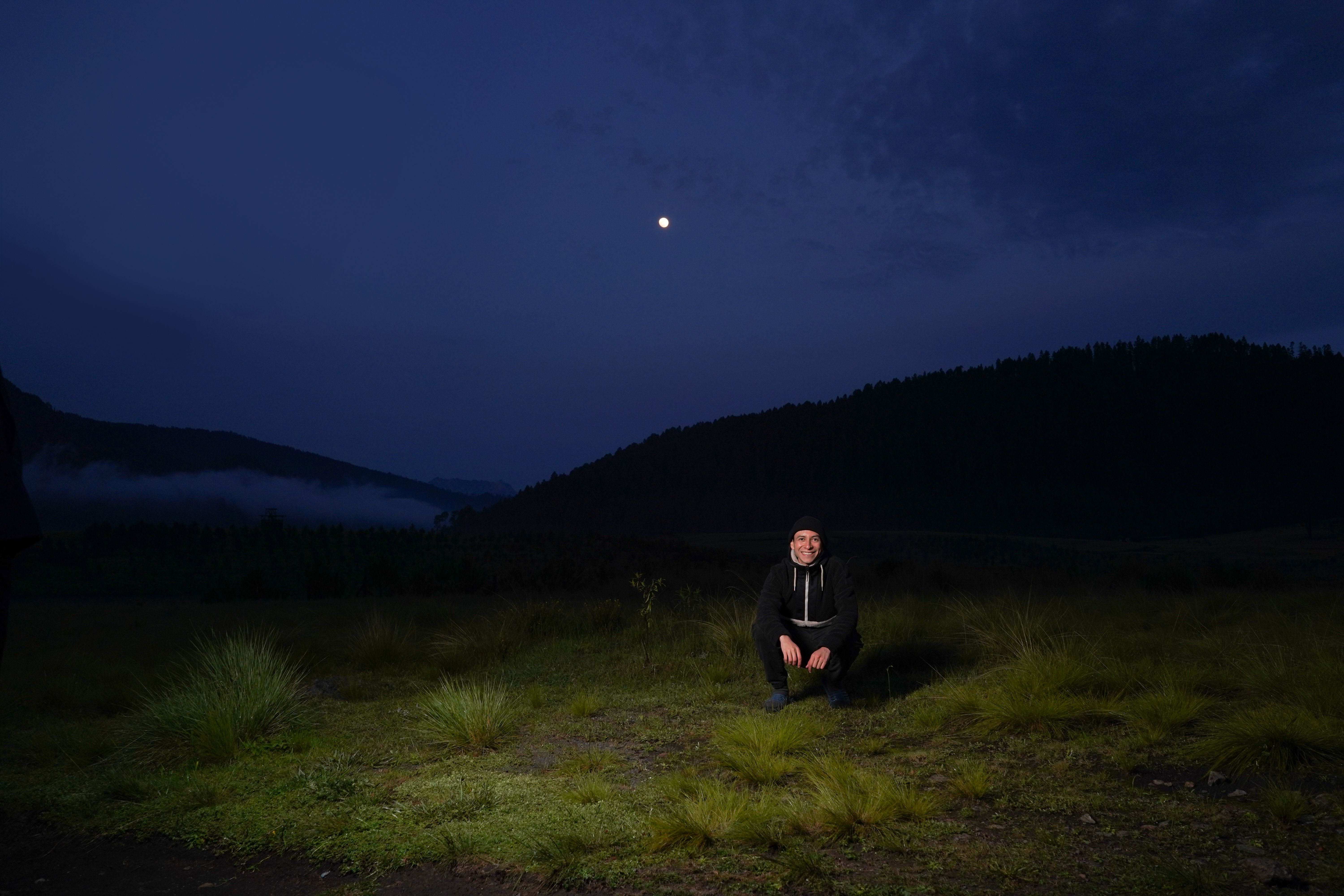 Person sitting in a grassy field under a clear moonlit night.