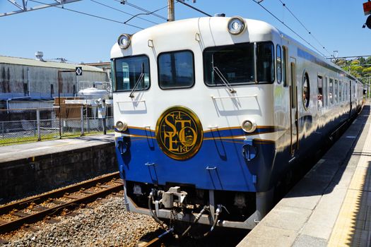 Luxury train at Kure Station, Hiroshima, Japan, under clear blue sky.