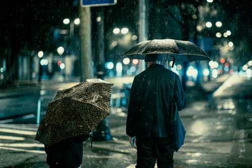 Free A moody city street at night with two people under umbrellas in the rain. Stock Photo