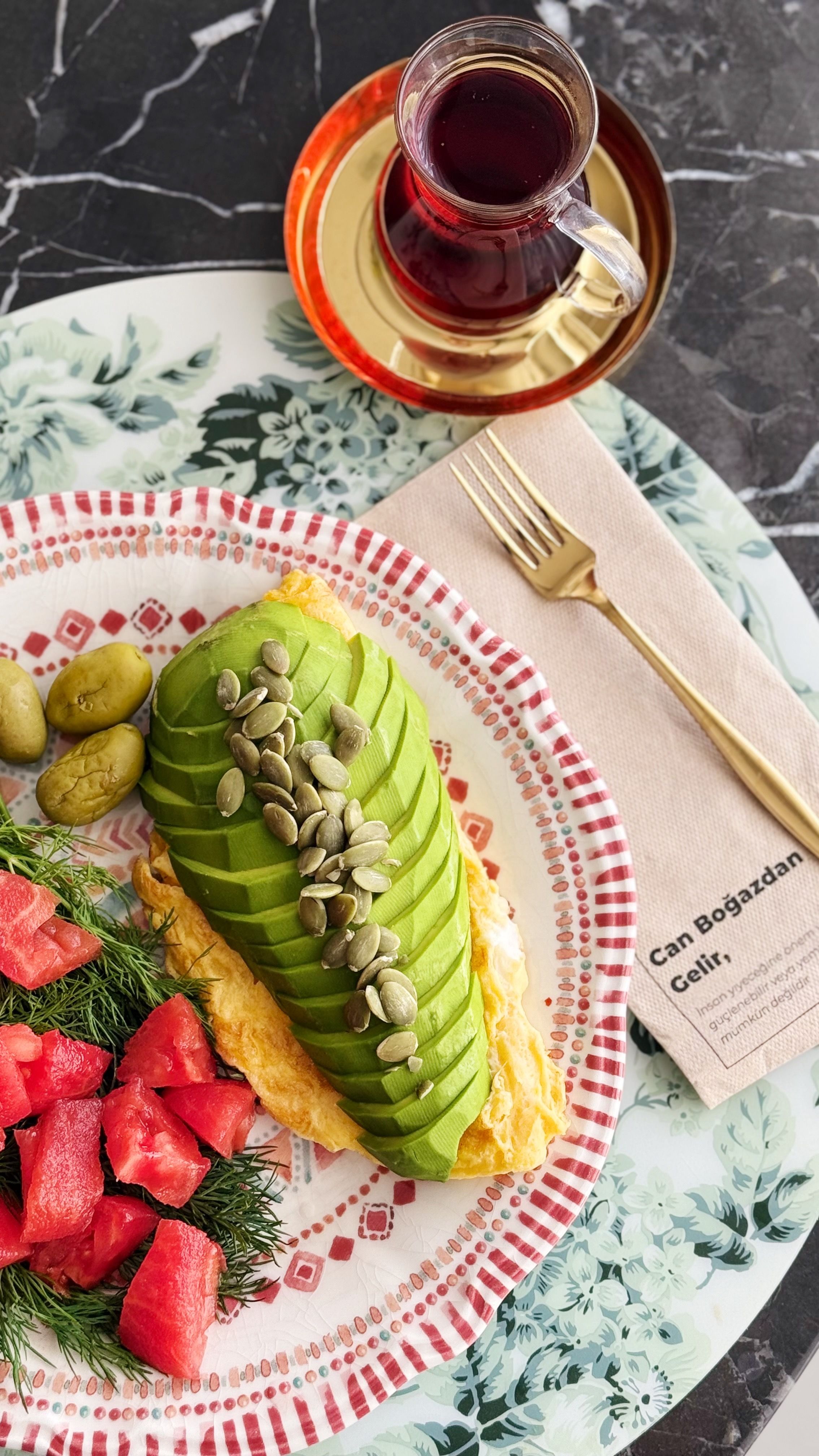 A colorful Turkish breakfast plate with avocado toast, olives, watermelon, and tea.
