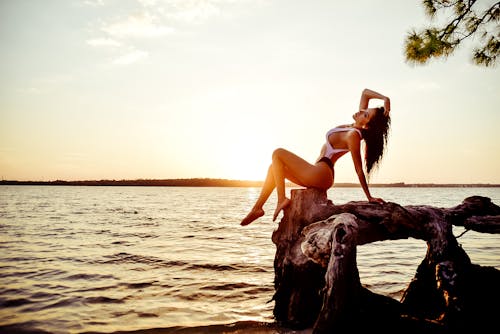 Woman in Black Bikini Sitting on Brown Rock Near Sea