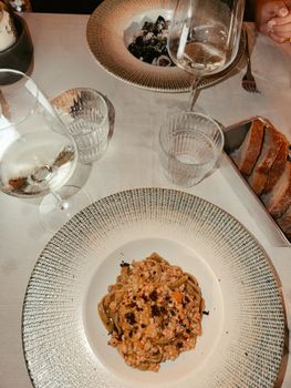 Overhead view of a gourmet Italian meal with pasta, wine, and bread on a table.