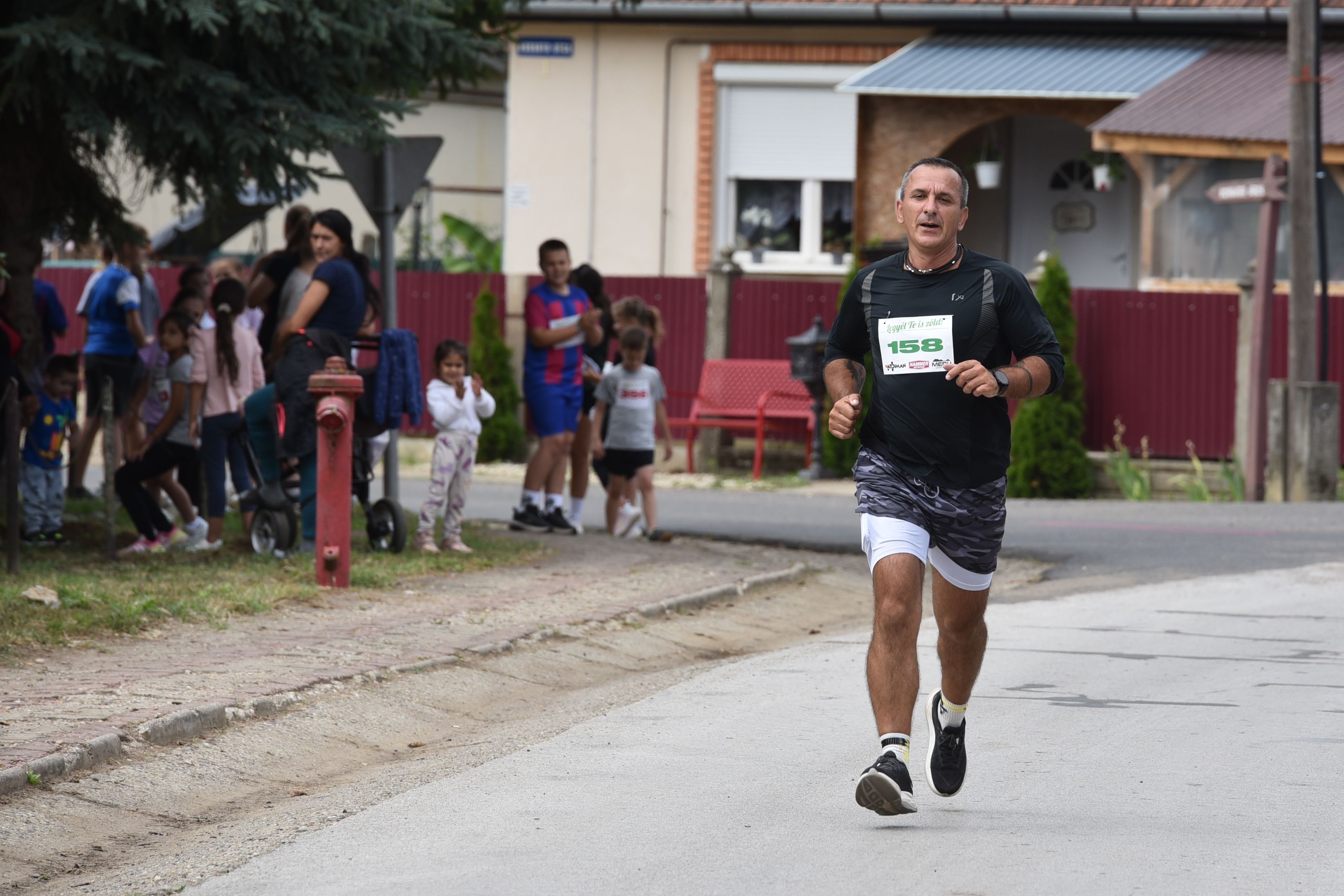 Athlete running in suburban marathon with spectators watching from sidewalk.