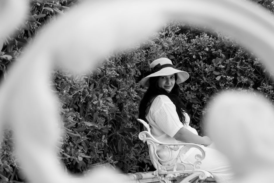 Black and white photo of woman in hat sitting in garden with foliage.
