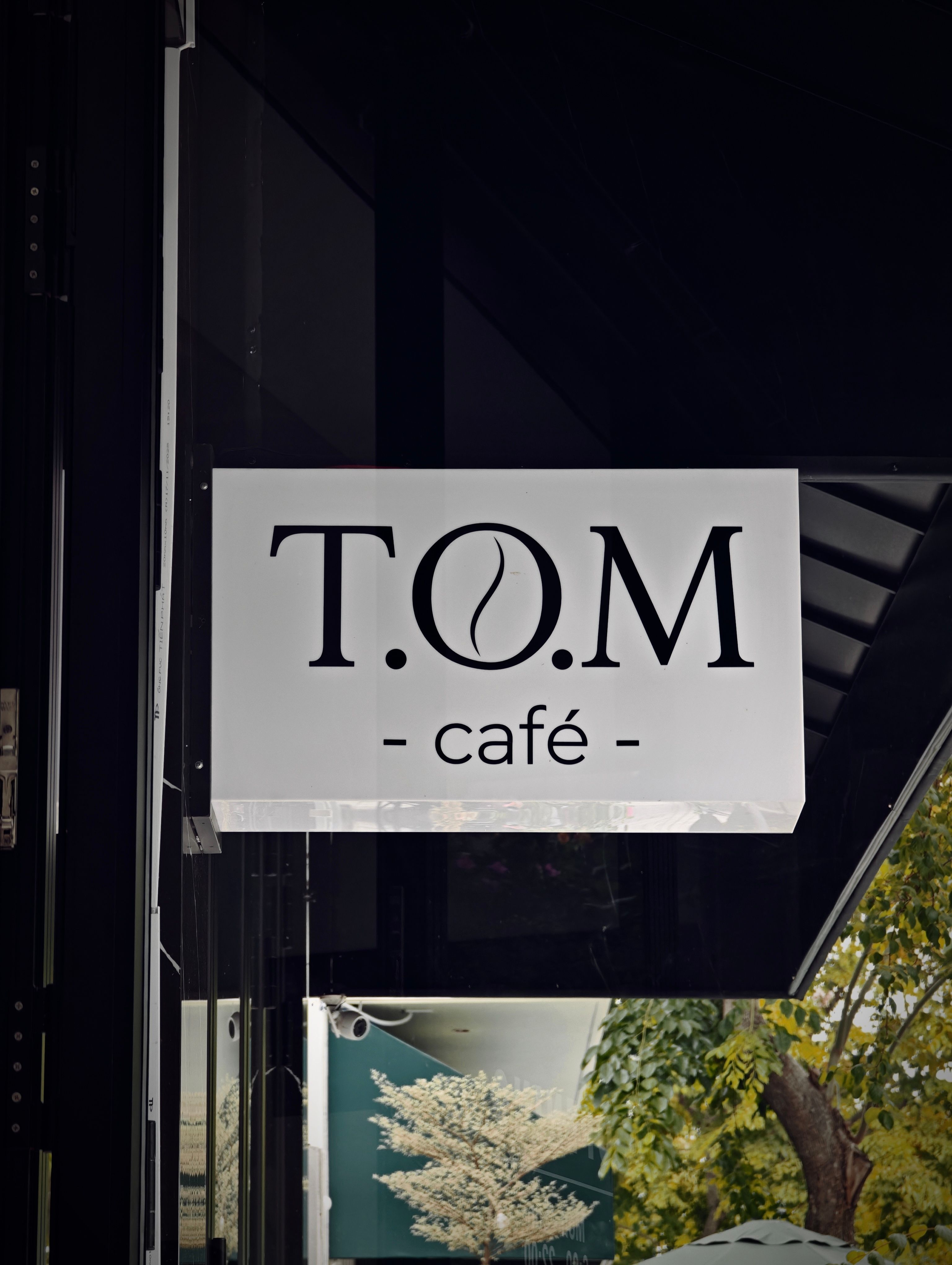 T.O.M Café sign with coffee bean design at an outdoor location.