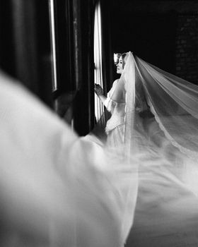 Graceful bride in Antalya captured in black and white, looking out a window with a long veil.