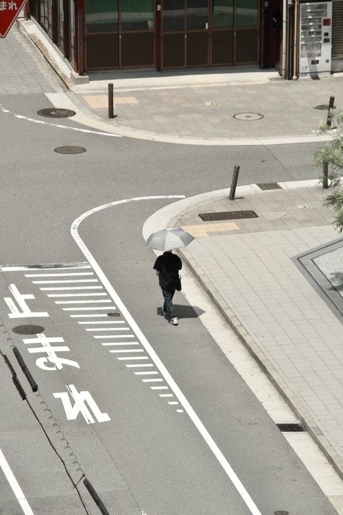 Free A person walks with an umbrella on a quiet street corner in Osaka, Japan, captured from above. Stock Photo
