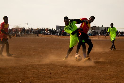 Action-packed scene of a community soccer game with players in vibrant jerseys on a dusty field., free online jigsaw puzzle on JigsawPuzzlesFreeOnline.org