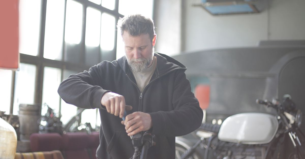 Foto de moto en Serious male mechanic in casual wear with gray beard standing in garage and fixing motorcycle steering wheel in back lit · ServiMotriz Villavicencio