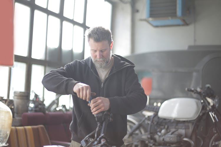 Bearded Man Repairing Motorcycle In Workshop