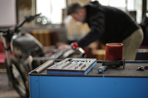 Plastic toolbox with small metal details placed on metal workbench in spacious garage while faceless adult  male mechanic repairing motorbike