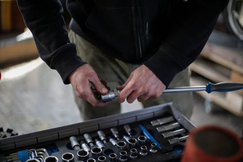 Unrecognizable crop adult male mechanic in black workwear installing metal socket on ratchet while working in modern workshop