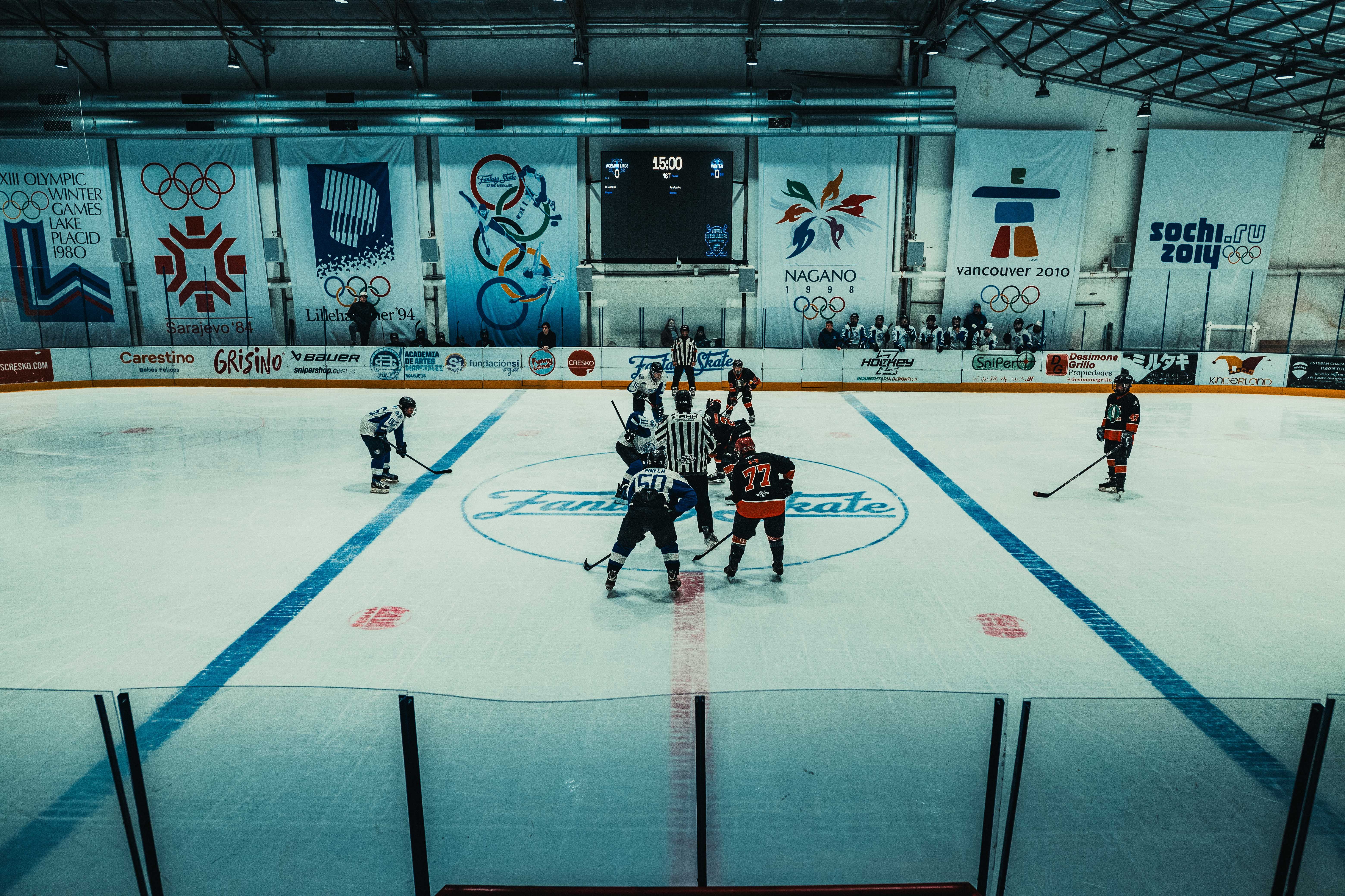 NCAA Basketball photo featuring Dramatic ice hockey face-off in an Olympic-themed indoor arena, capturing the spirit of the sport.