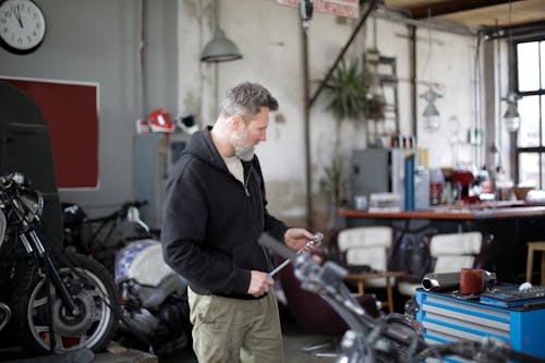 Side view of serious middle aged male mechanic in workwear standing with ratchet in modern garage while repairing motorbike