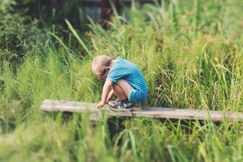 Free Child in striped outfit sitting on wood in grassy field, capturing peaceful innocence. Stock Photo