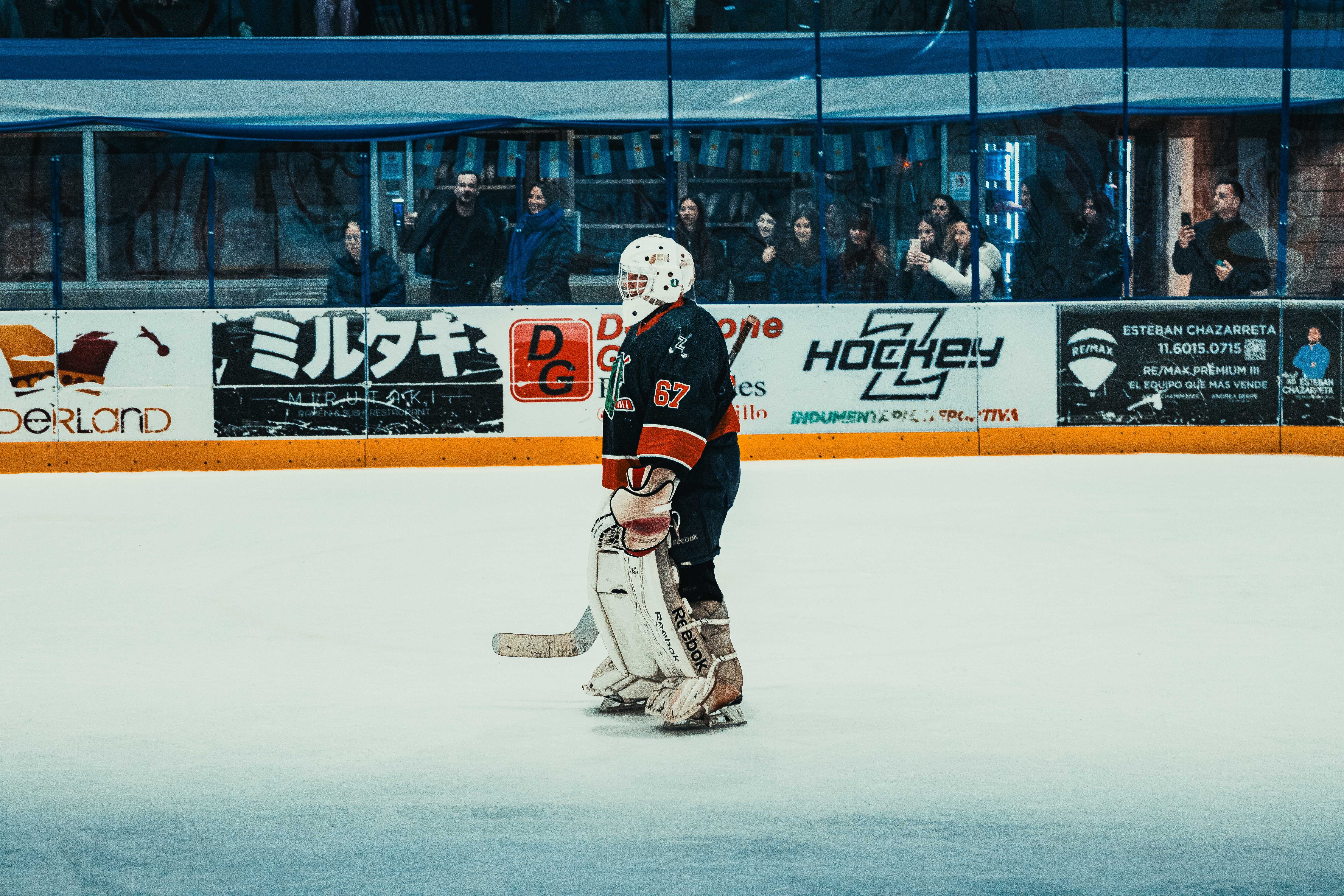 NBA photo featuring Intense ice hockey scene with goalie in action at Buenos Aires rink. Enthusiastic spectators in the background.