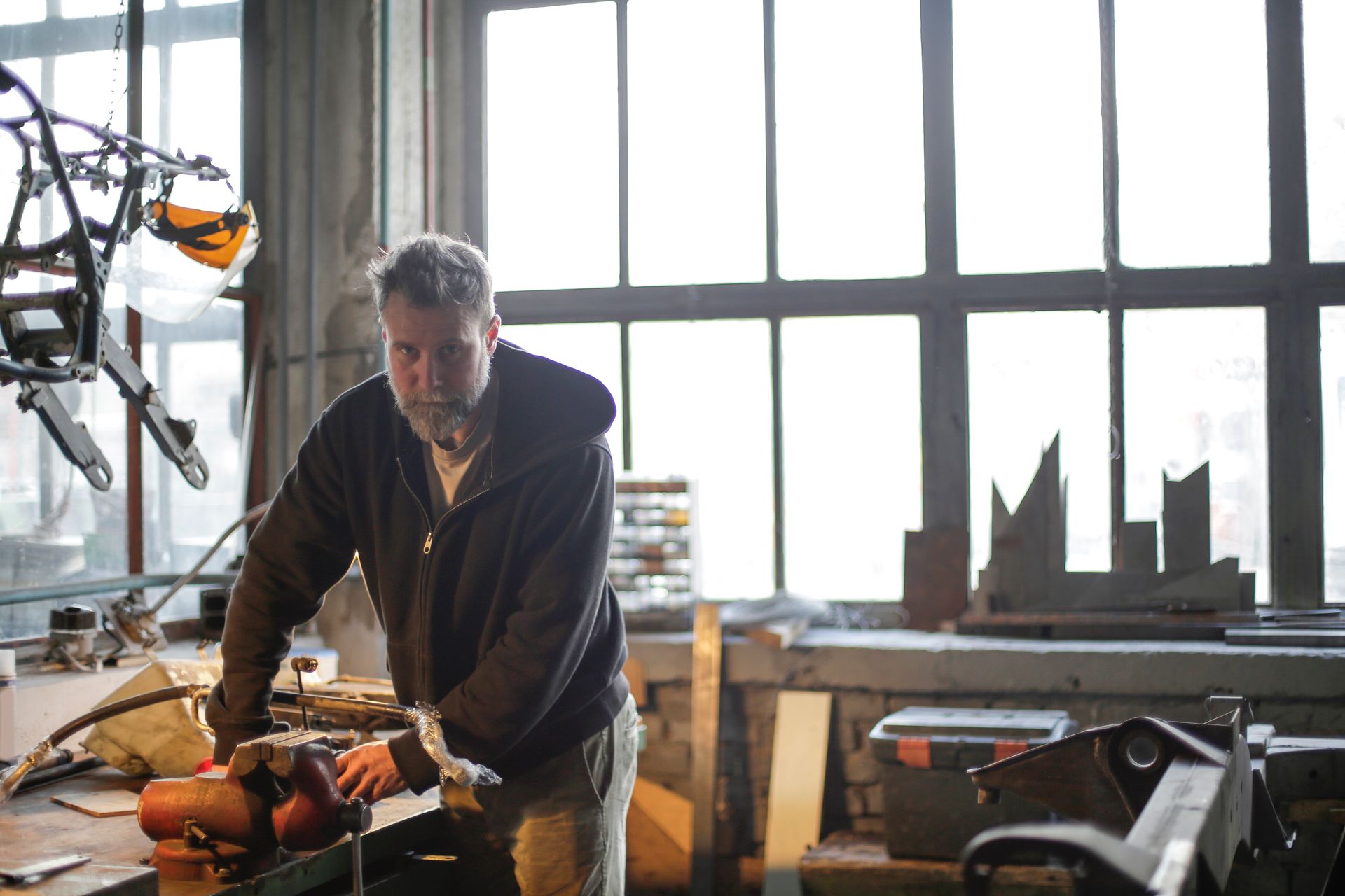 A bearded man concentrates on a repair task in a well-lit workshop, surrounded by tools.